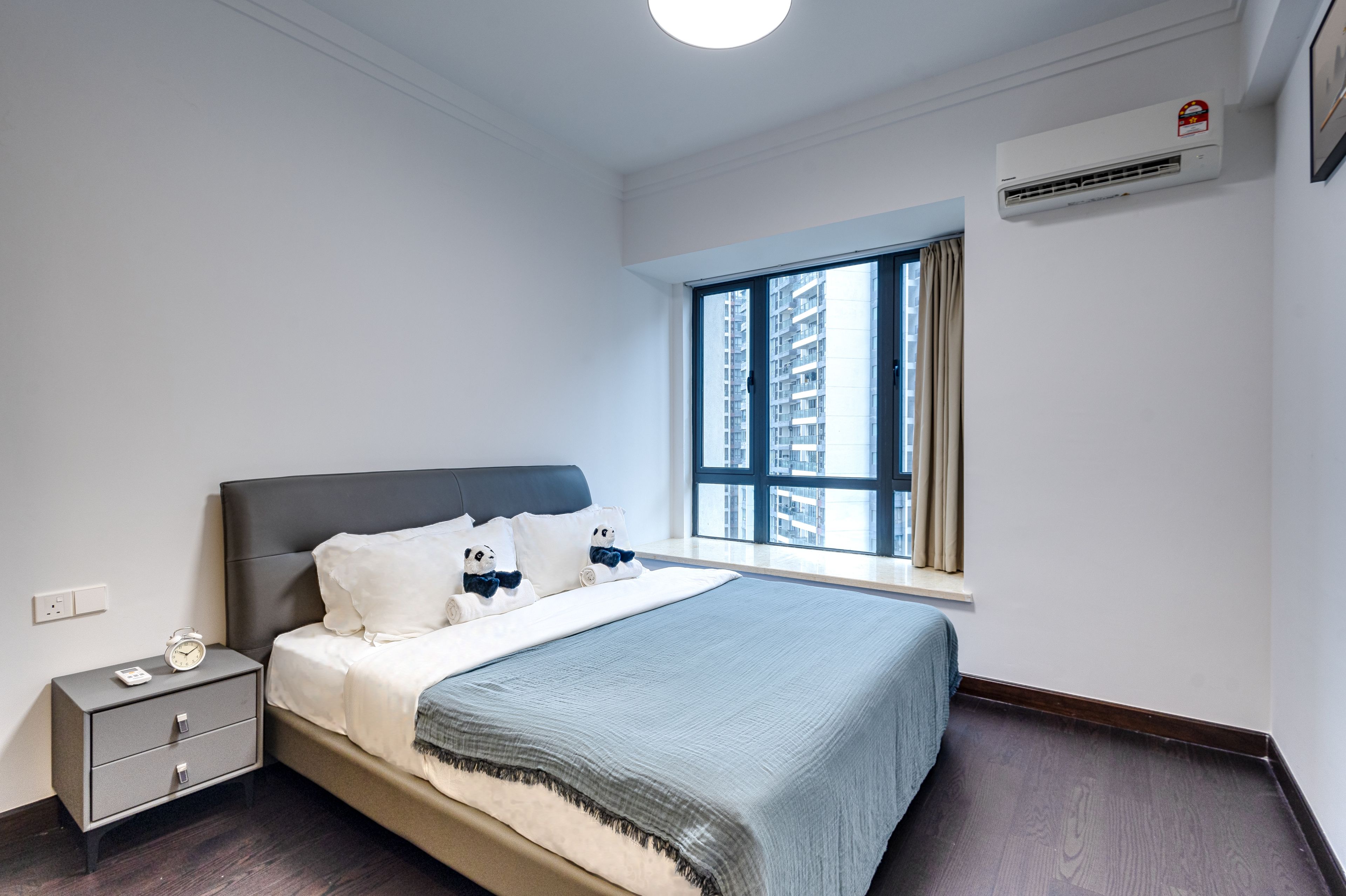 Un dormitorio con cama, mesita de noche y ventana con vistas a edificios.