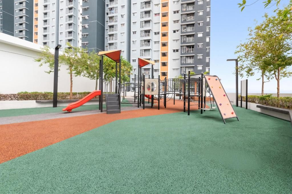 Un parque infantil con un tobogán y estructuras de escalada, rodeado de césped y un edificio al fondo.