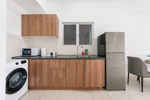 A modern kitchen with wooden cabinets, a stainless steel refrigerator, a washing machine, and a window above the sink.