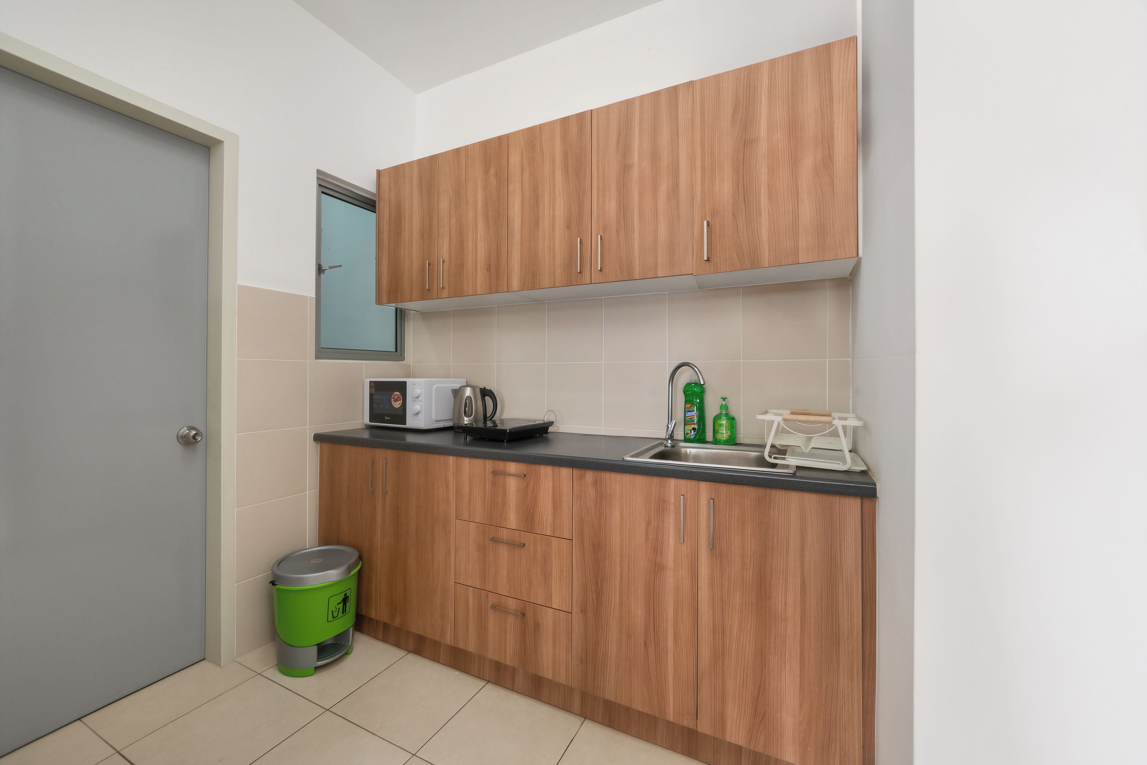 Una cocina compacta con armarios de madera, un microondas, una tetera y un cubo de basura.