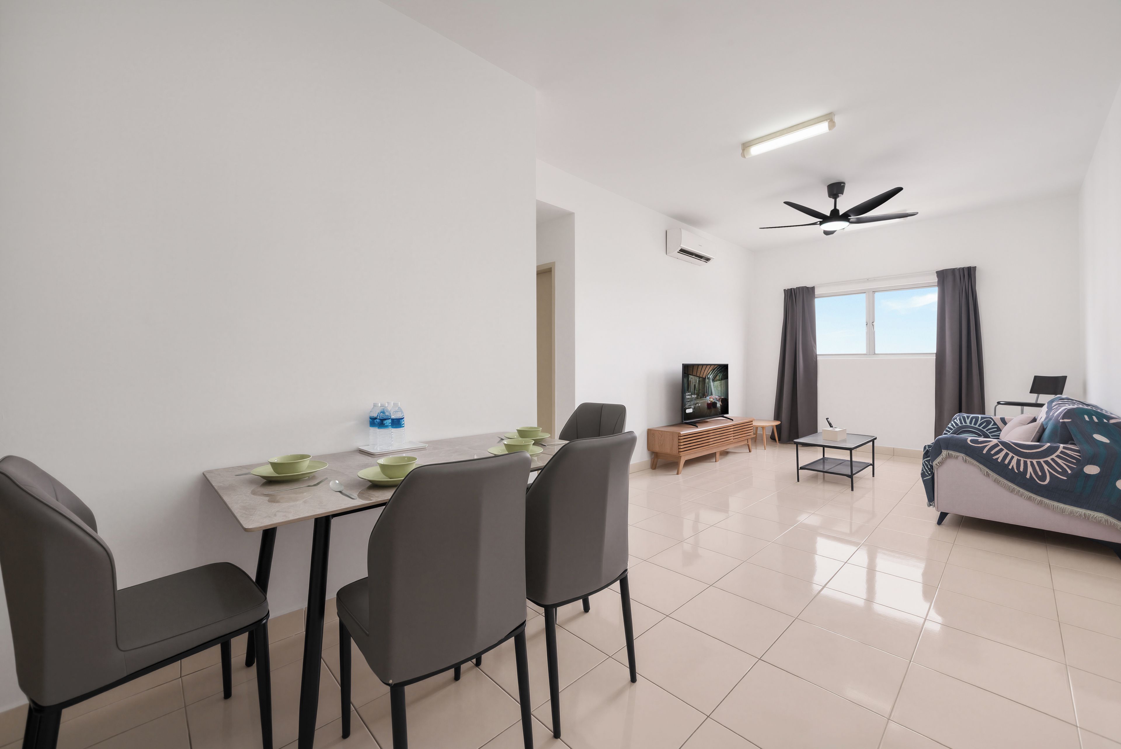 A modern living room with a dining area, a flat-screen TV, a ceiling fan, and a large window with curtains.