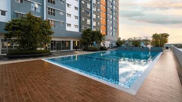 Piscina en la azotea con vistas a un edificio de varios pisos, rodeada de árboles y una terraza de madera.