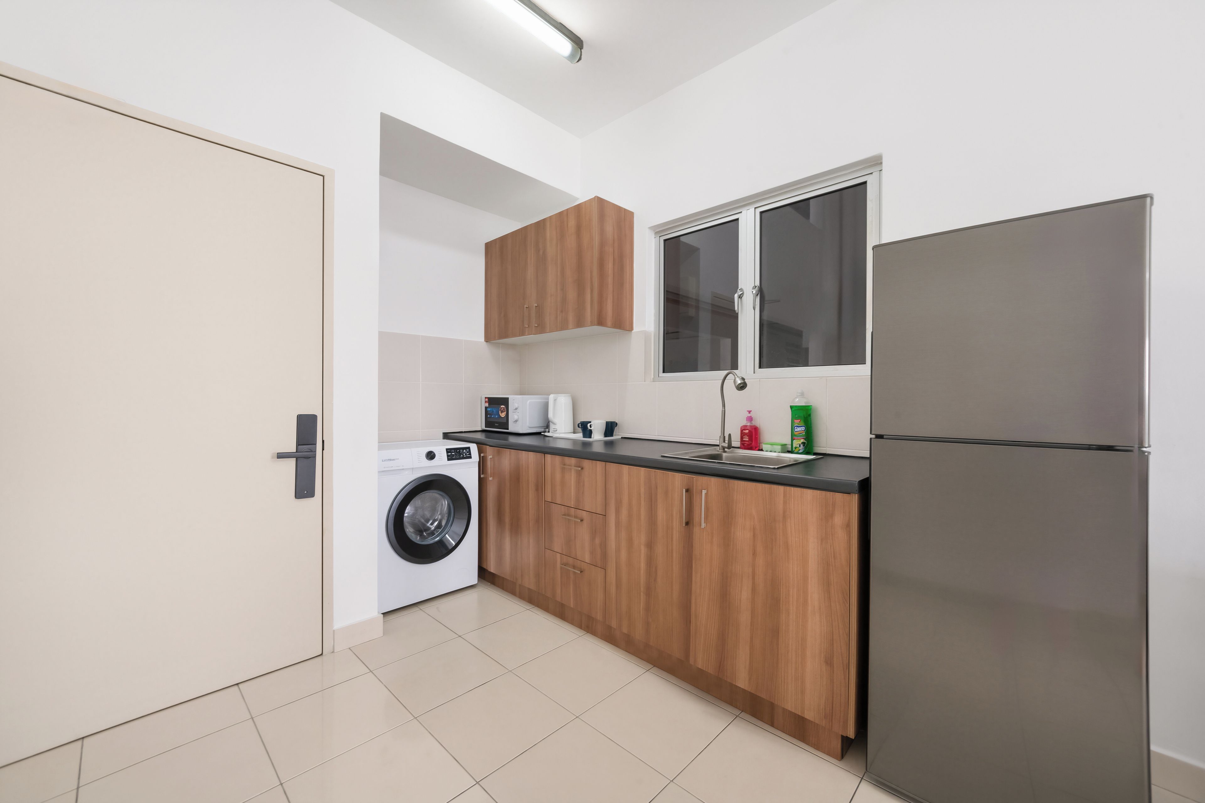 A compact kitchen with a washing machine, a refrigerator, wooden cabinets, and a window.