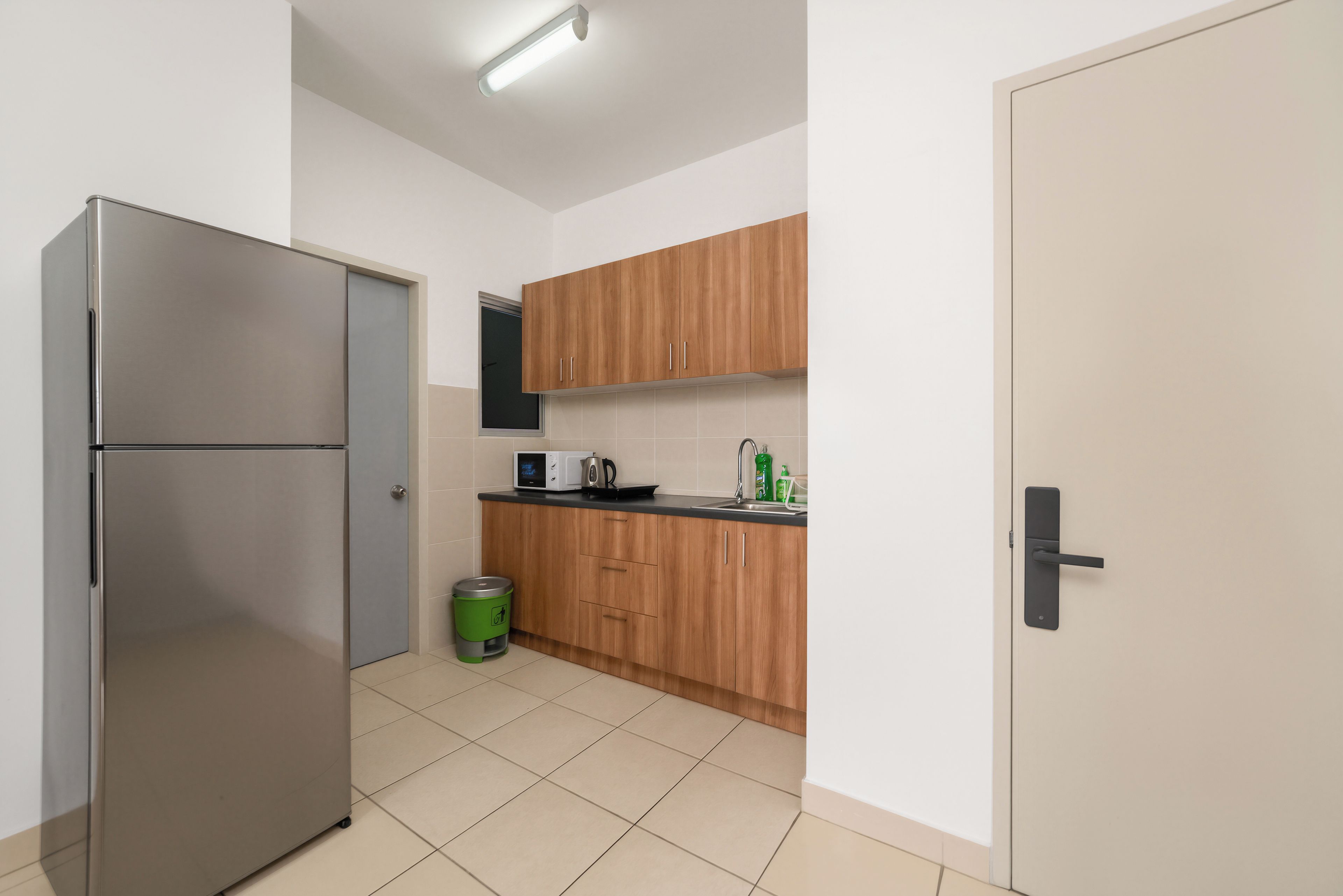 Una cocina funcional con un refrigerador de acero inoxidable, armarios de madera, un microondas y un lavamanos.
