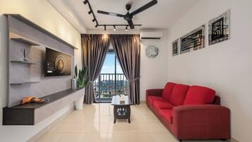 Una sala de estar moderna con un sofá rojo, un televisor de pantalla plana, un ventilador de techo y vistas a edificios a través de amplios ventanales.