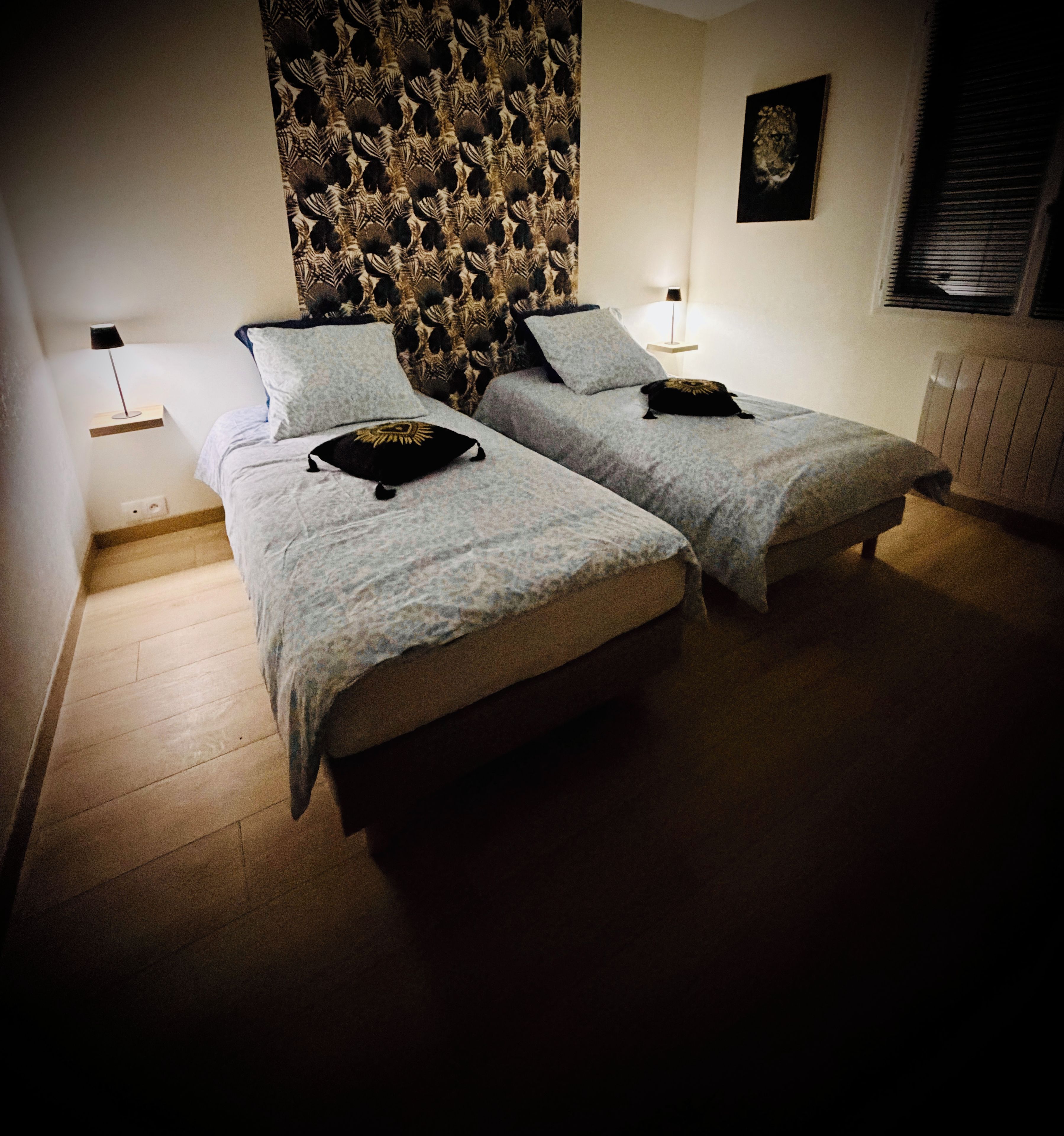 A room with two beds, a patterned headboard, a framed picture on the wall, and a window with blinds.