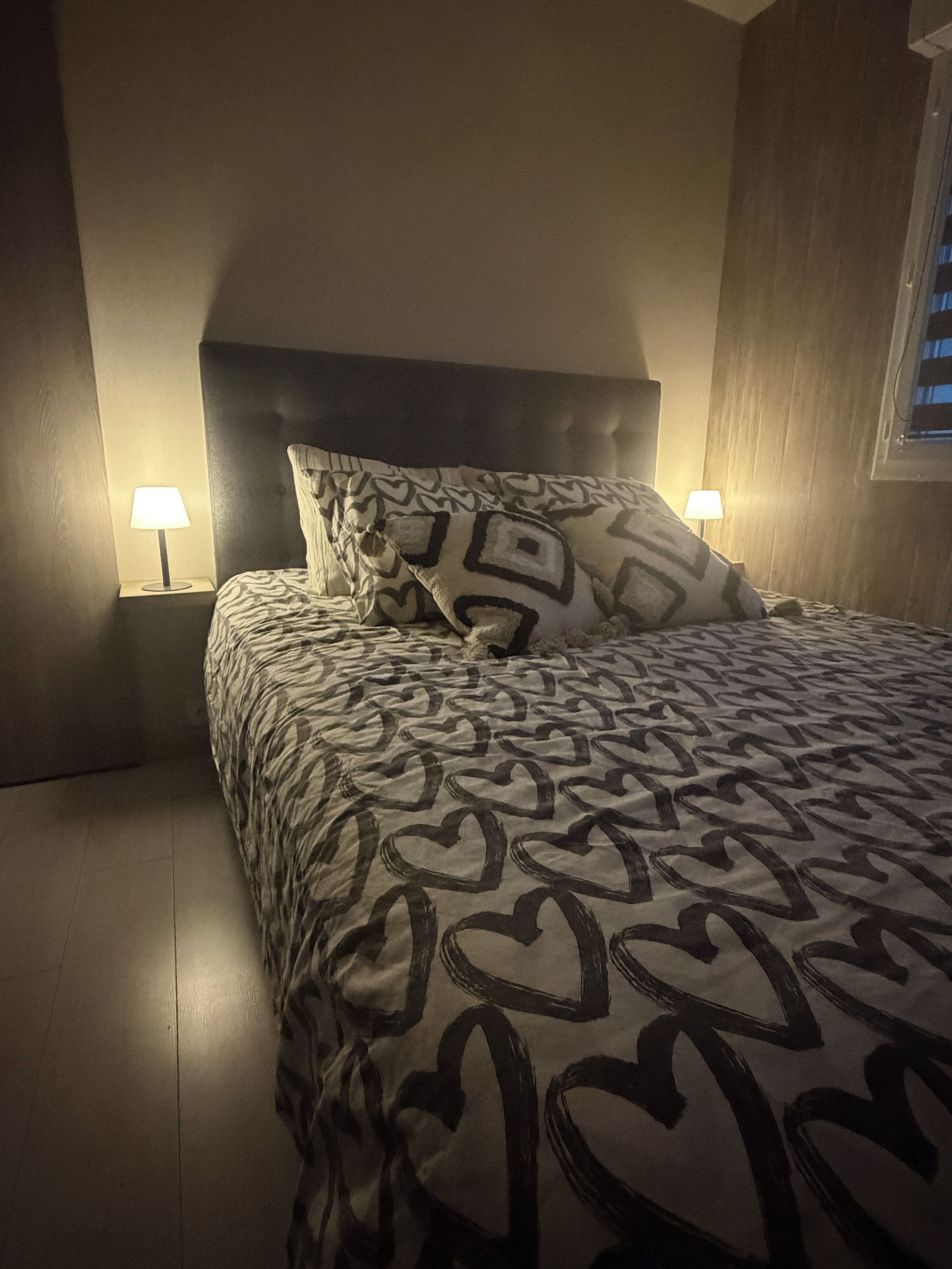 A bedroom with a patterned bedspread, two bedside lamps, and a wooden headboard.