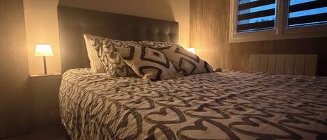 A bedroom with a bed, a nightstand, a lamp, and a window with blinds.