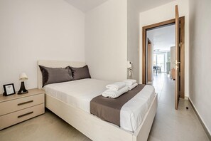 Een hotelkamer met een bed, nachtkastje, lamp en uitzicht op de gang.