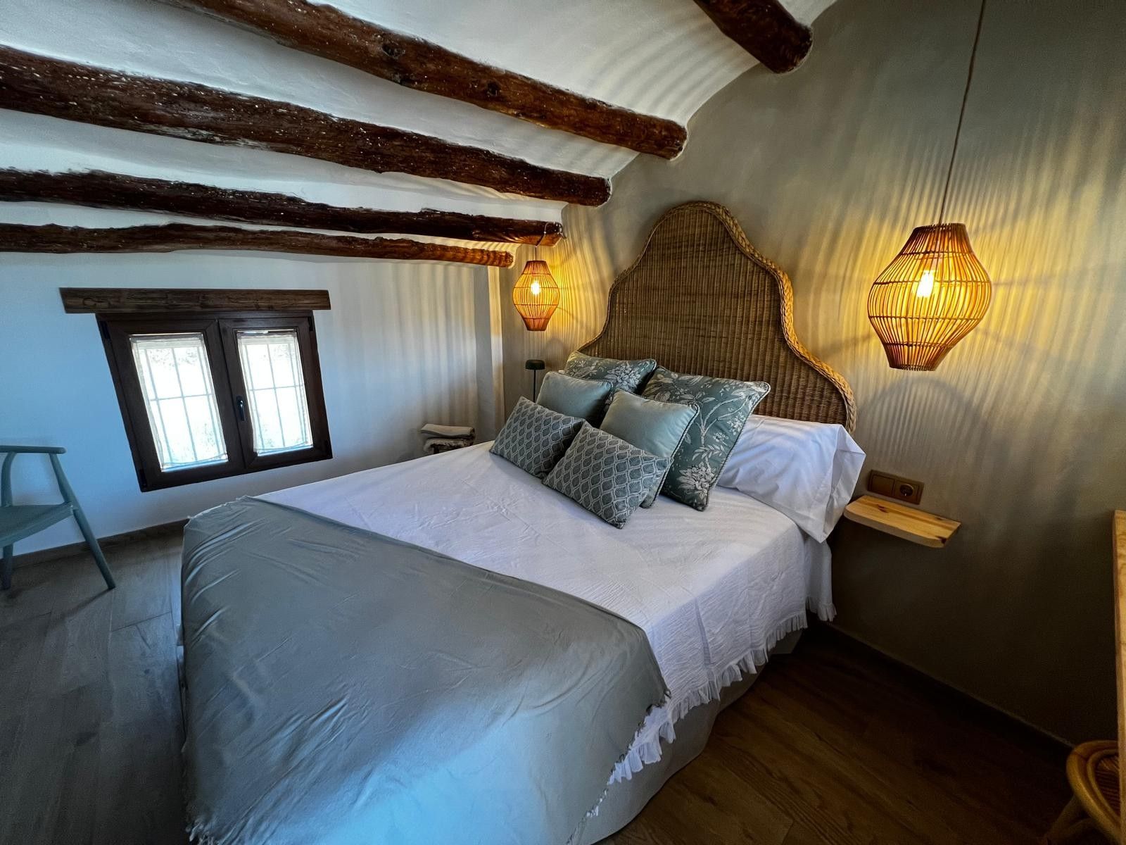 A bedroom with a large bed, two bedside lamps, a window, and a wooden ceiling.