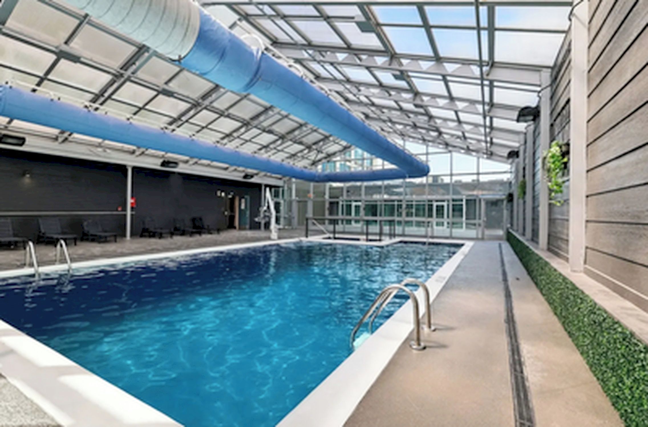 An indoor swimming pool with clear glass walls, a blue ceiling, and a tiled floor.