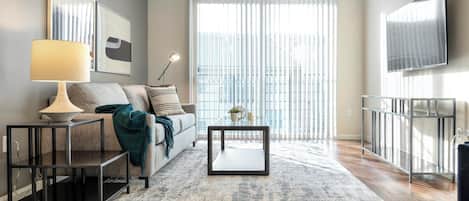 A modern living room with a sofa, coffee table, lamp, and a large window with blinds.