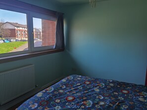 Un dormitorio con ventana, radiador y cama con colcha estampada.
