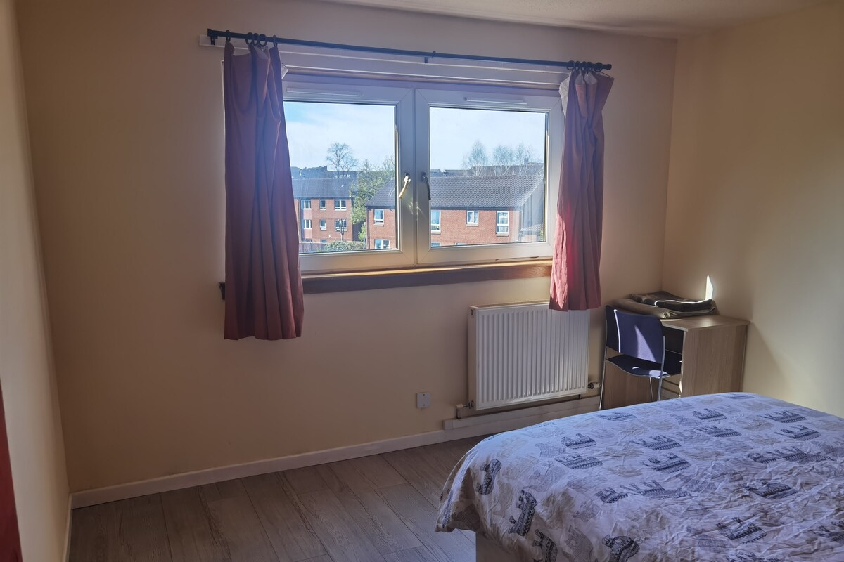 Un dormitorio con cama, un radiador, televisor y ventana con cortinas.