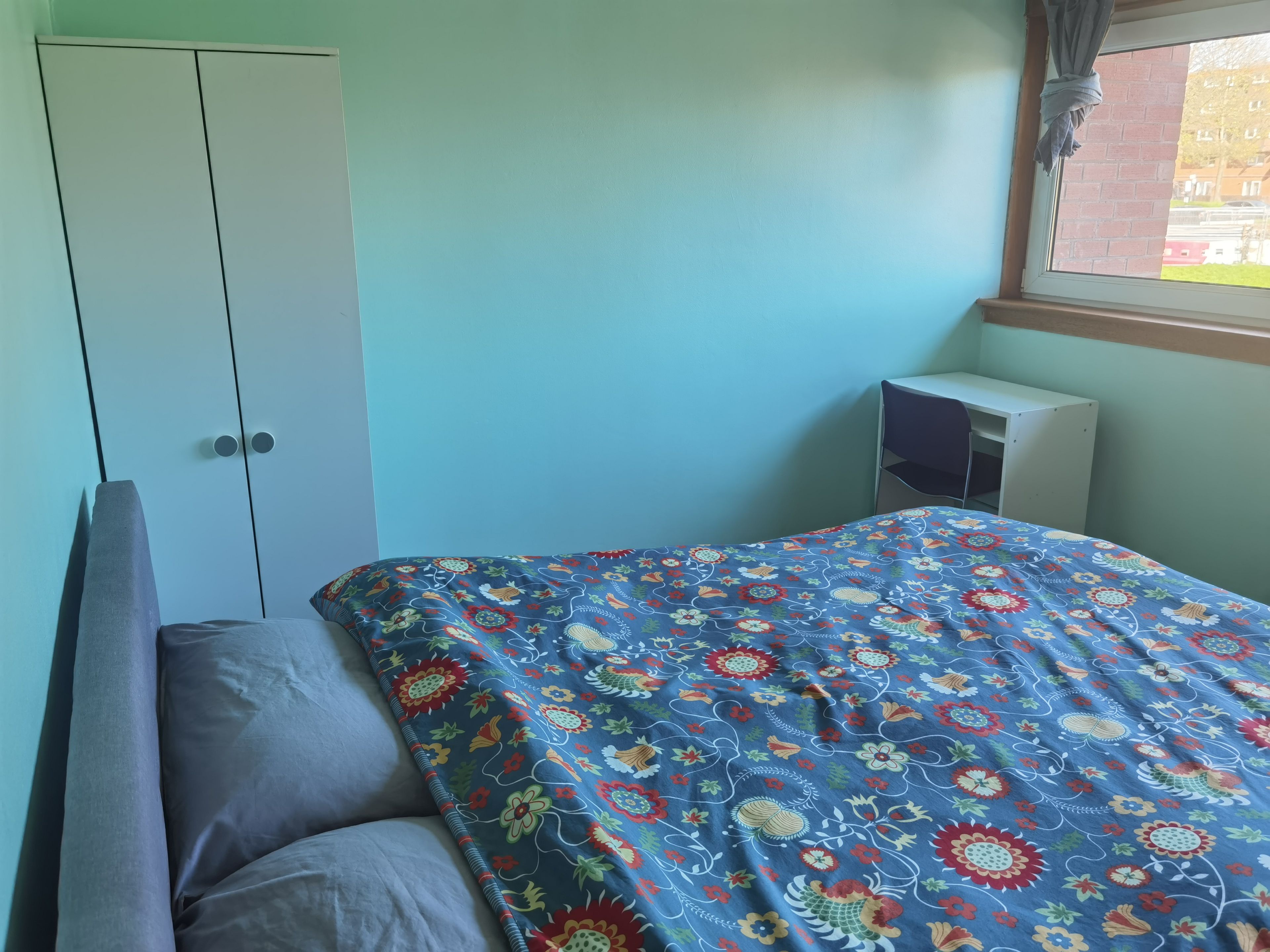 A bedroom with a bed, a wardrobe, a desk, and a window.