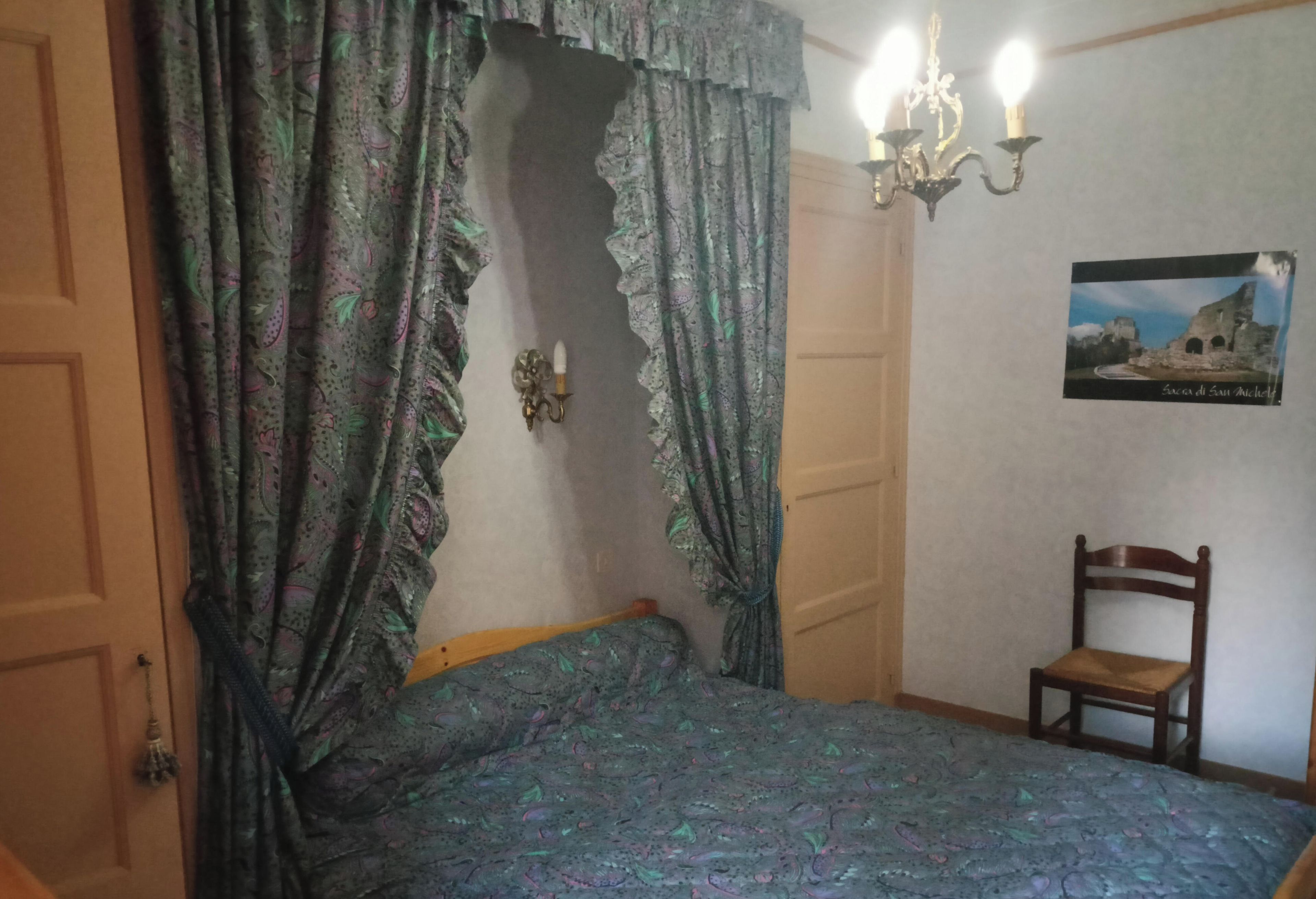 Een slaapkamer met een bed, een stoel, een wandlamp en een lijst met een afbeelding.