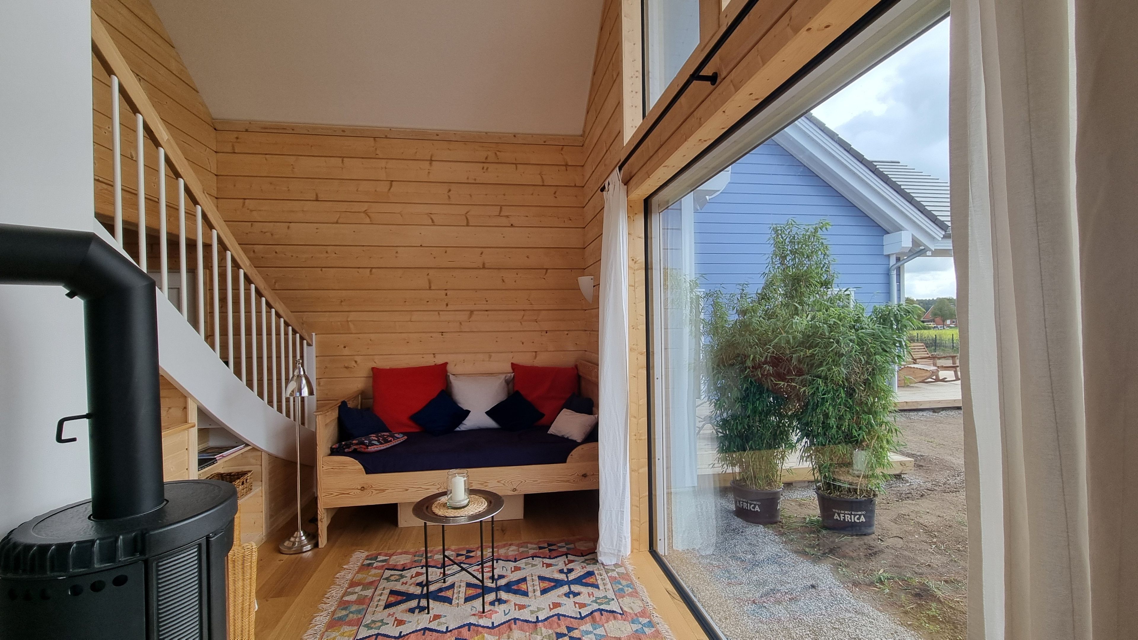 Ein gemütliches Zimmer mit Holzbalkendecke, einer Couch mit Kissen, einem kleinen Tisch und einem Fenster mit Blick ins Freie.
