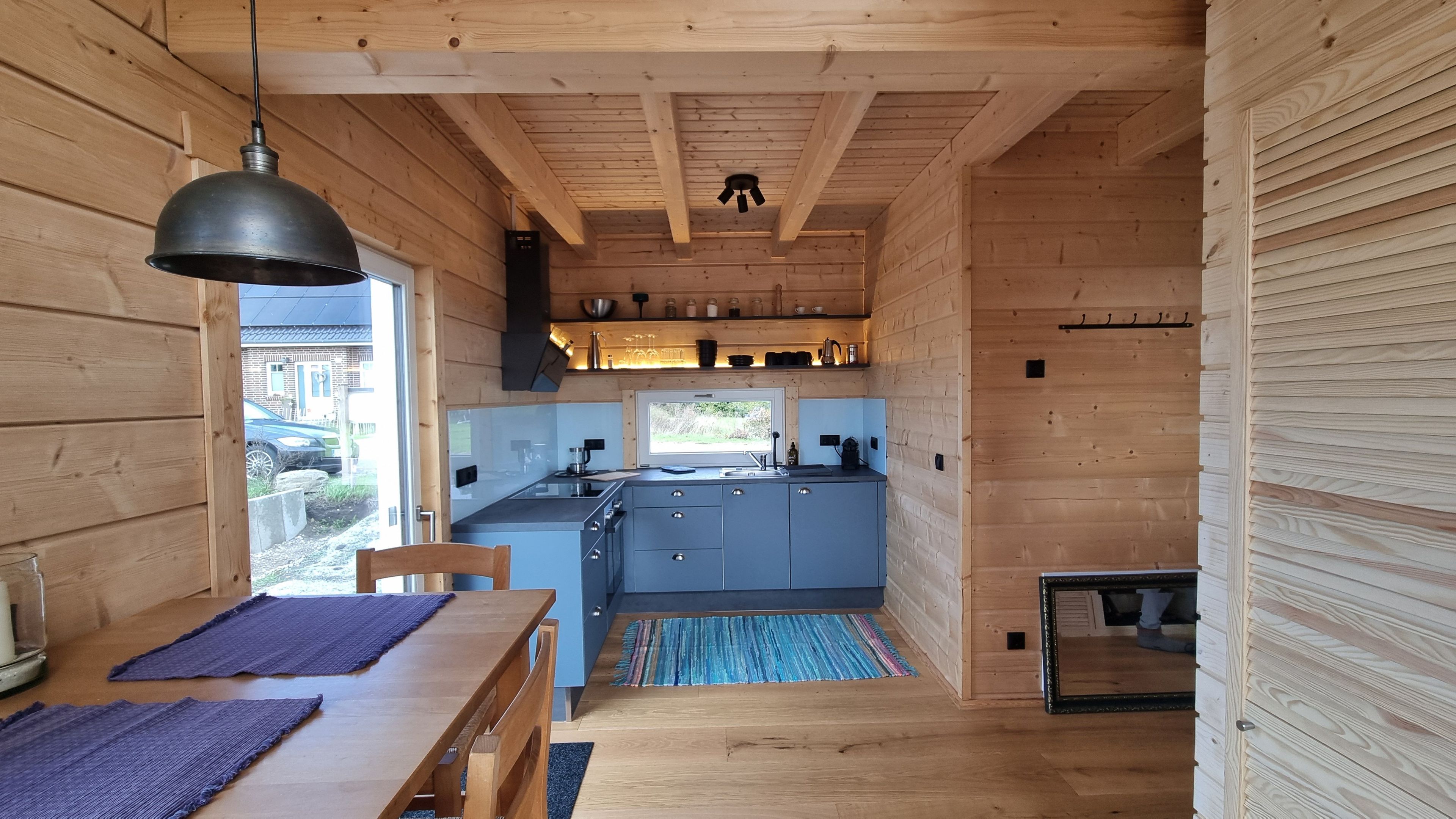 Eine kleine Küche mit Holzwänden, einer zentralen Kochinsel und einem Fenster mit Blick auf einen Garten.