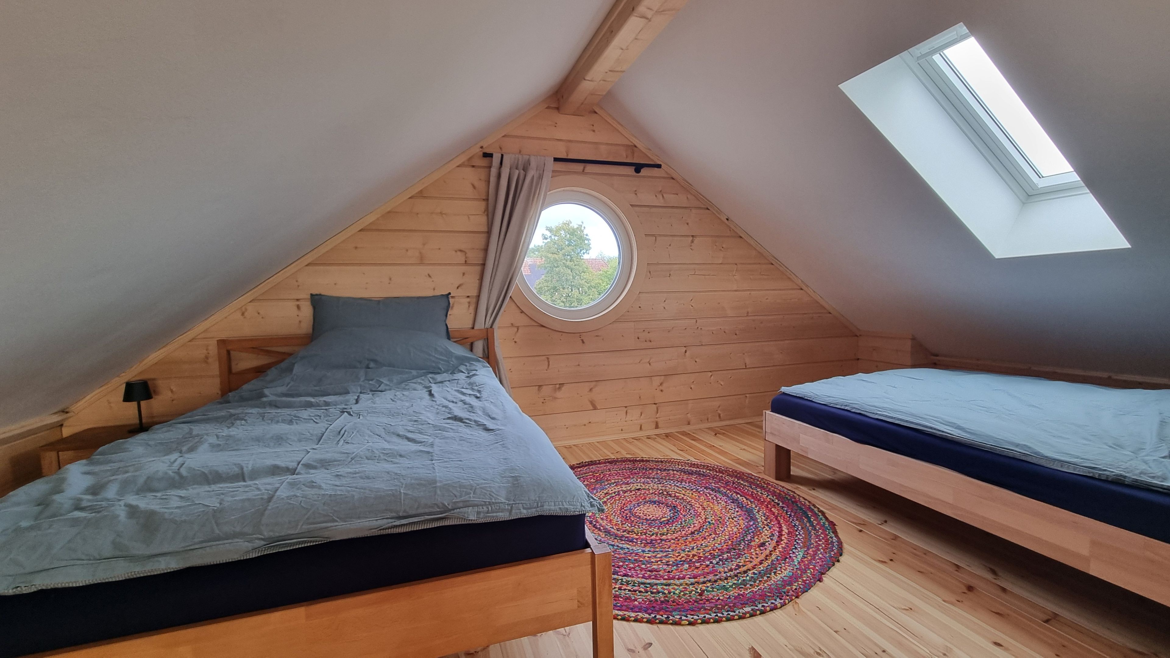 Ein kleines Schlafzimmer im Dachgeschoss mit zwei Betten, einem Oberlicht und einem Rundfenster.