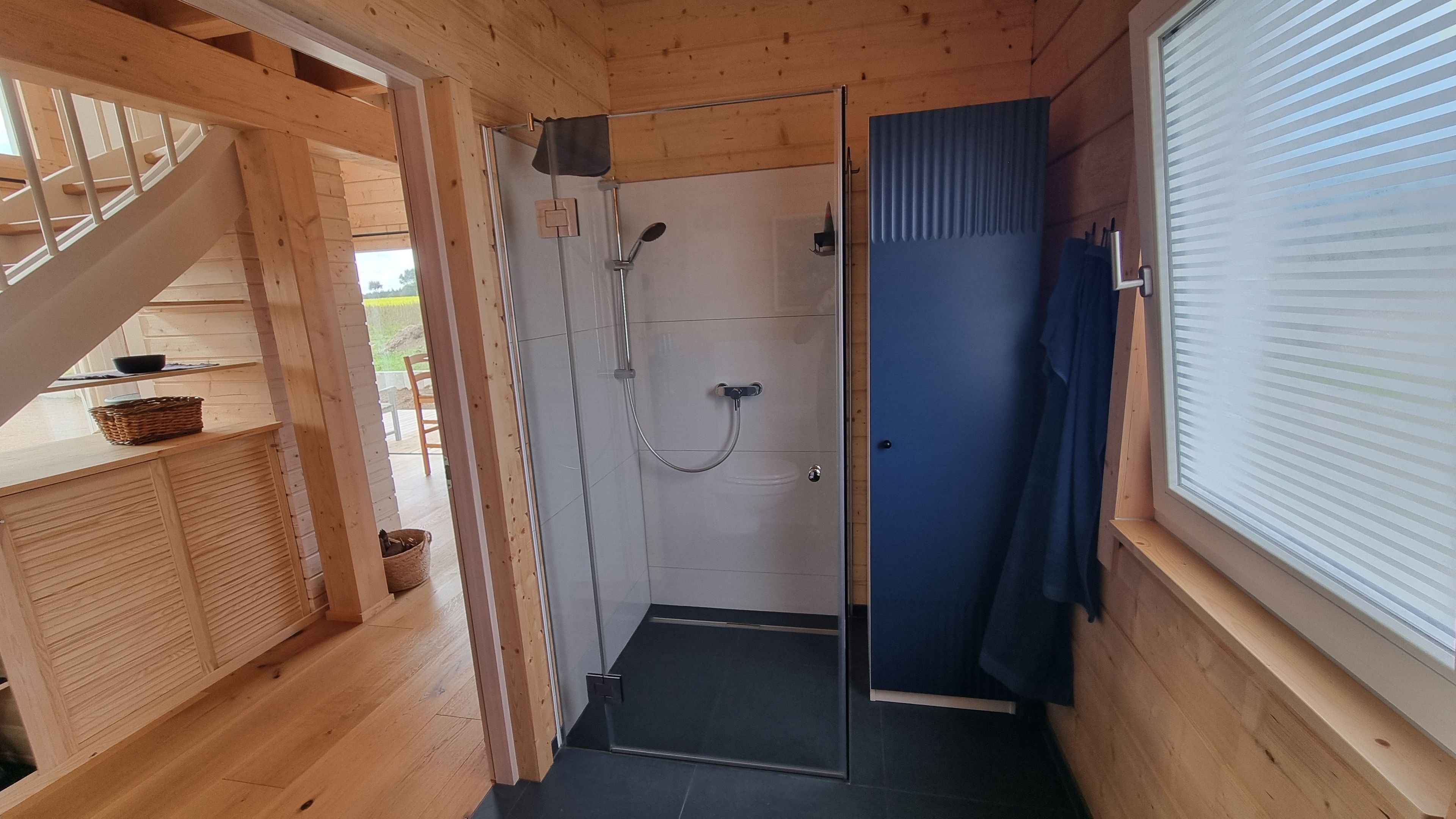Eine Holzhütte mit einer Duschkabine, einer Holztreppe und einem Fenster mit Jalousien.