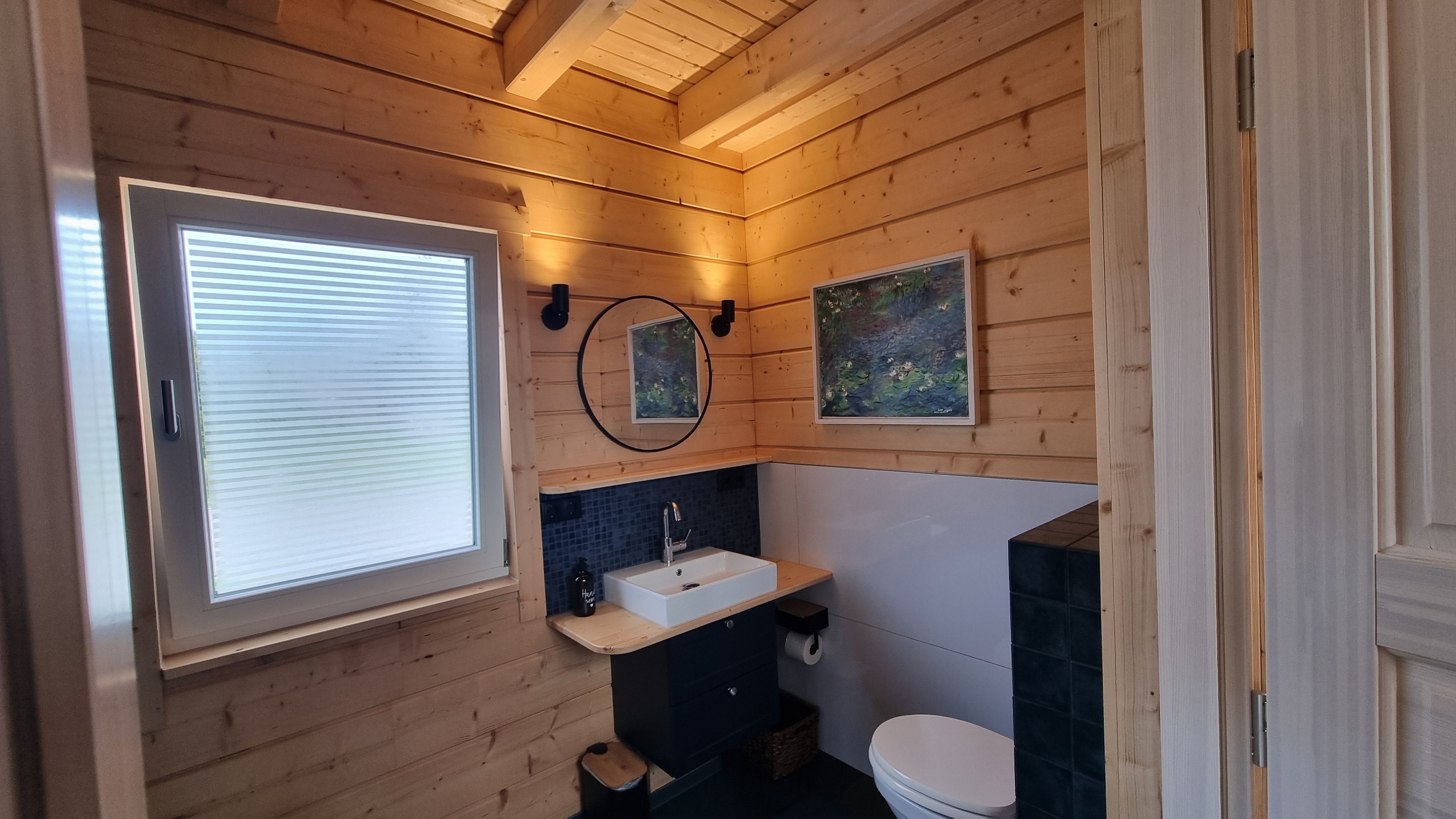 A wooden-paneled bathroom with a window, a sink, a toilet, and a mirror.