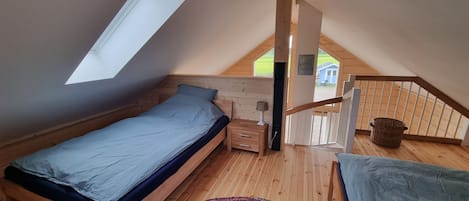 Ett sovrum med ett sluttande tak, en säng, ett nattduksbord, en lampa, en färgglad matta och utsikt över omgivningen.