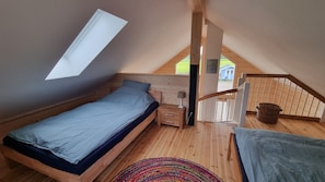 Quarto com teto inclinado, cama, mesa de cabeceira, abajur, tapete colorido e vista para o exterior.