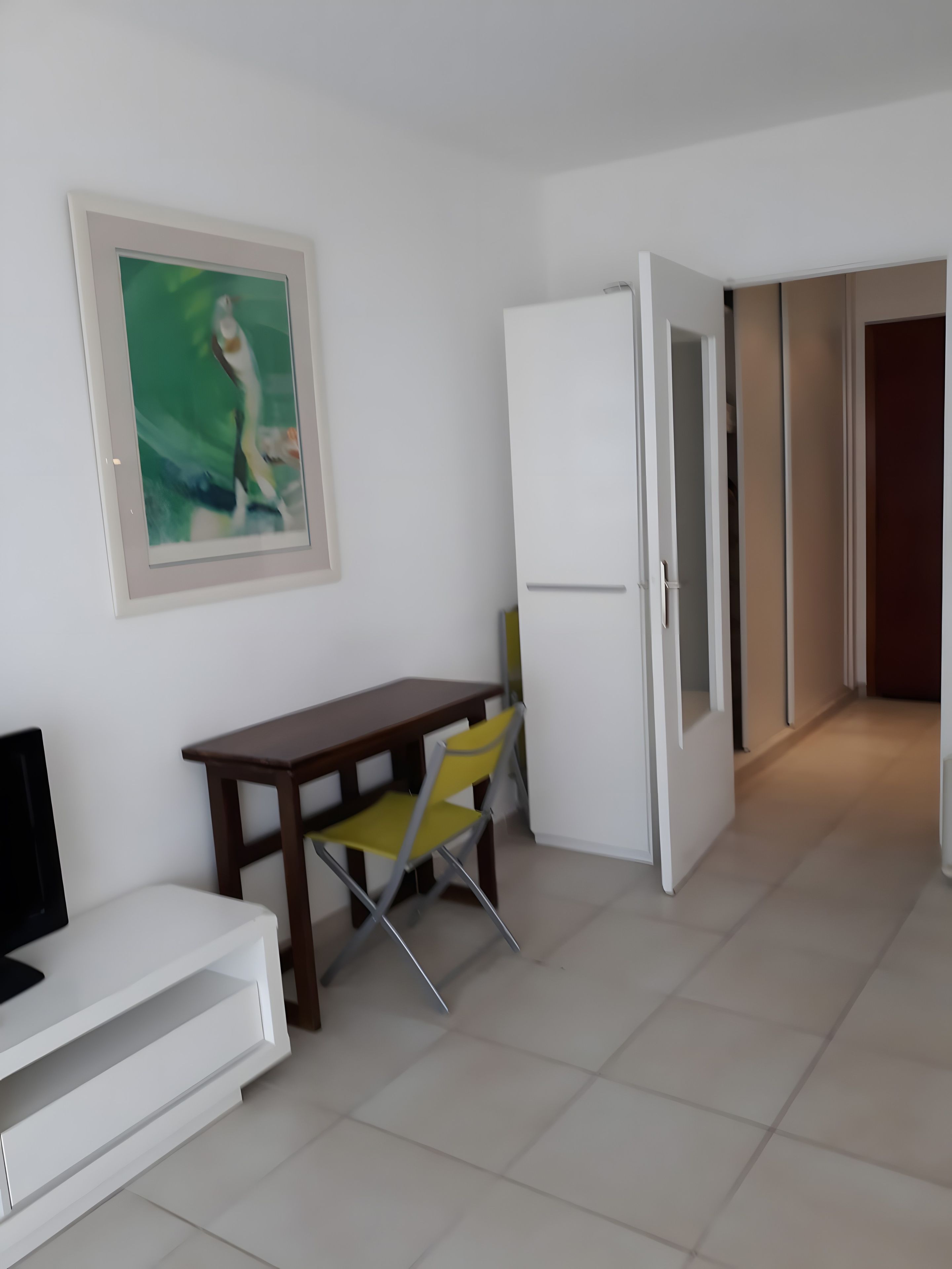 A room with a white sofa, a wooden table with a yellow chair, a white cabinet, and a white door leading to another room.