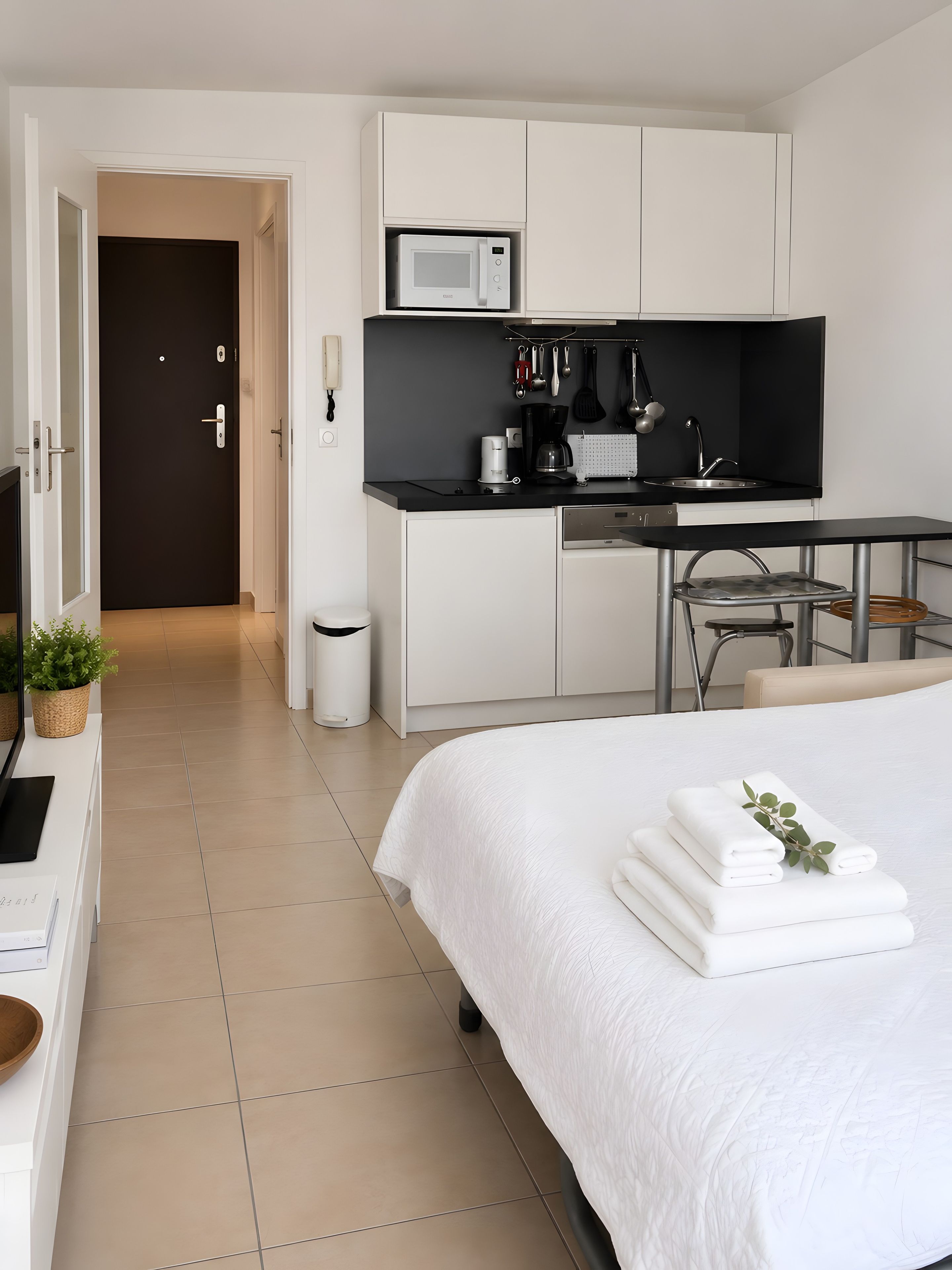 A modern hotel room with a bed, a kitchenette, a desk, and a bathroom.