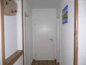 Un couloir avec une porte blanche, un plancher en bois et un tableau accroché au mur.