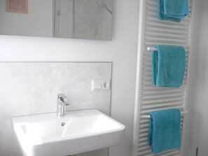 Ein Badezimmer mit einem weißen Waschbecken, einem Spiegel und einem Handtuchhalter mit blauen Handtüchern.