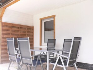 Eine Terrasse mit einem Glastisch und vier Stühlen, einem Holzzaun und einem Fenster mit Jalousien.