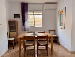 Uma área de refeições com mesa e cadeiras de madeira, uma janela com vista, um armário e um quadro na parede.