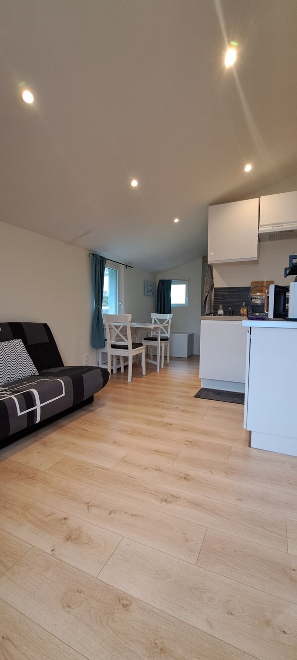A modern living room with a sofa, dining table, and chairs, a kitchenette, and a view of the sky. - Holiday Home 'Ty Melen' with Shared Terrace, Shared Garden and Wi-Fi (Locmiquélic)