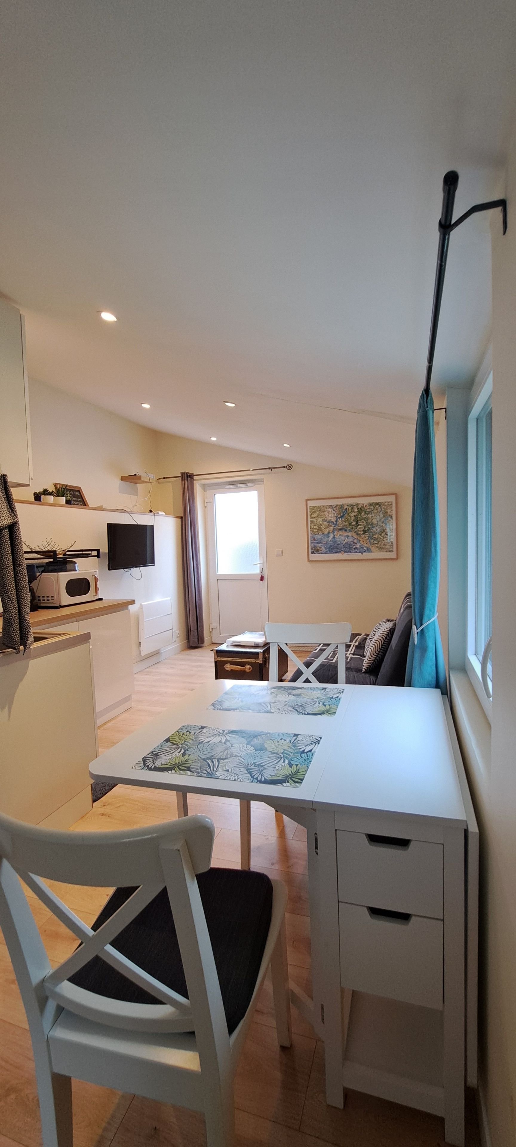 Un espacio habitable compacto con kitchenette, comedor y ventana con cortinas.