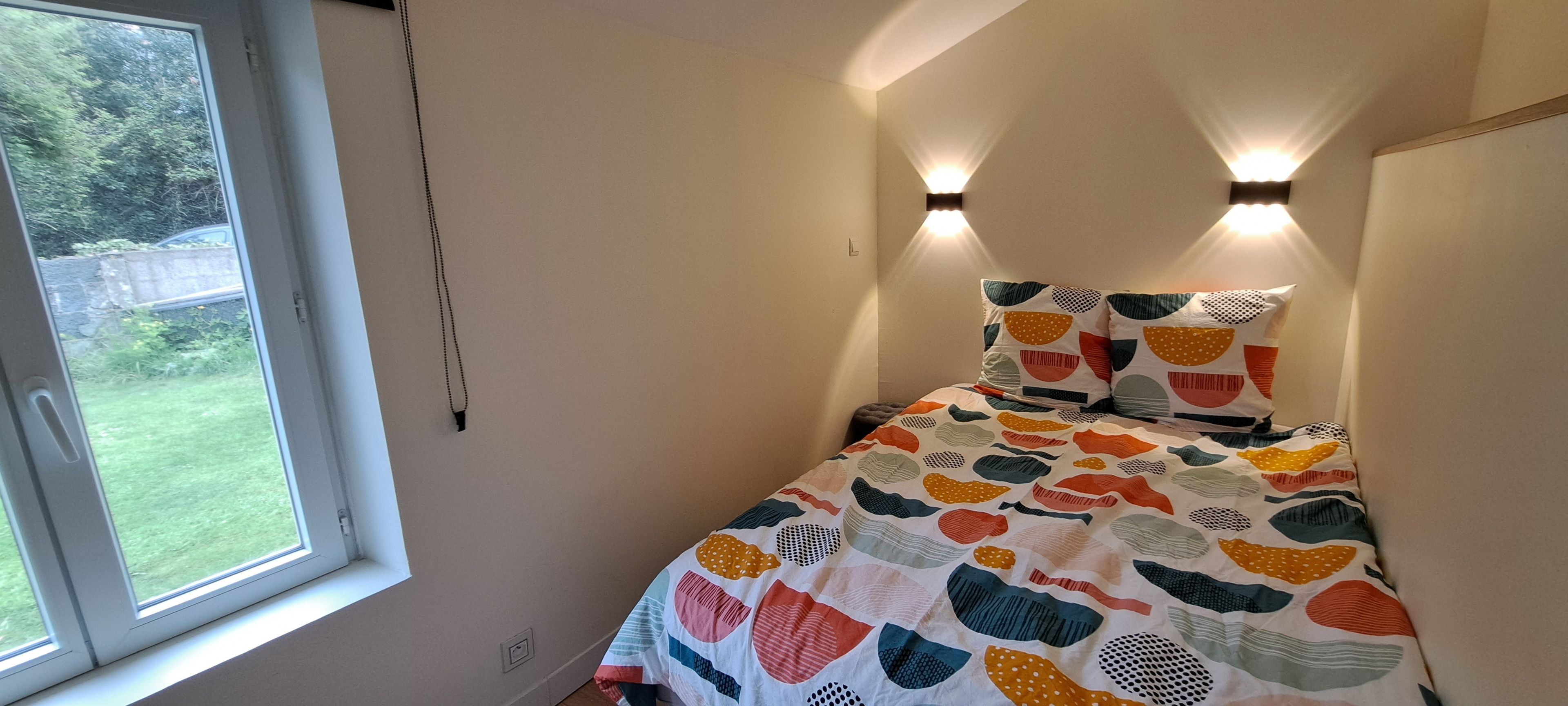 Ein Schlafzimmer mit einem Bett, einem Fenster und zwei Wandleuchten.