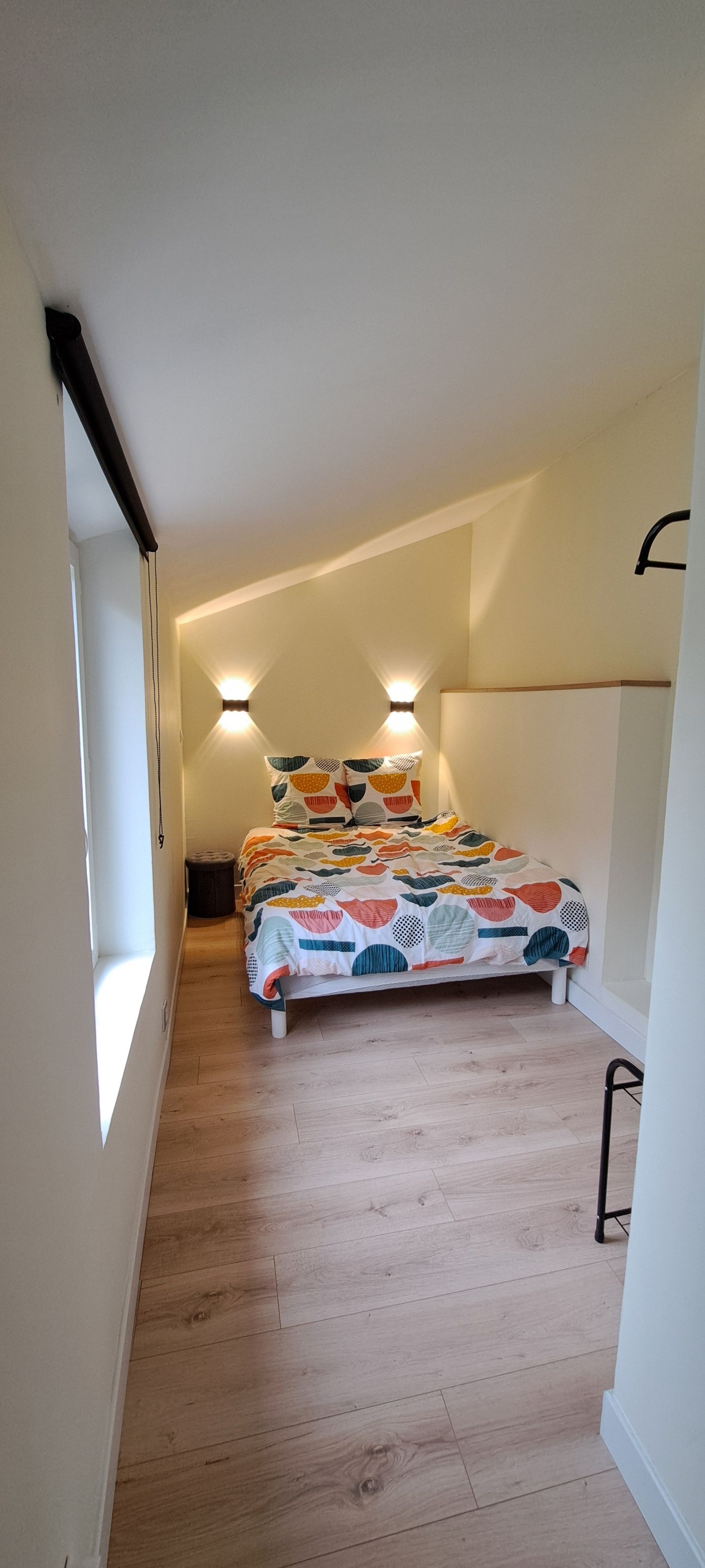 Une chambre à coucher avec un lit, un plancher en bois et deux lampes fixées au mur.