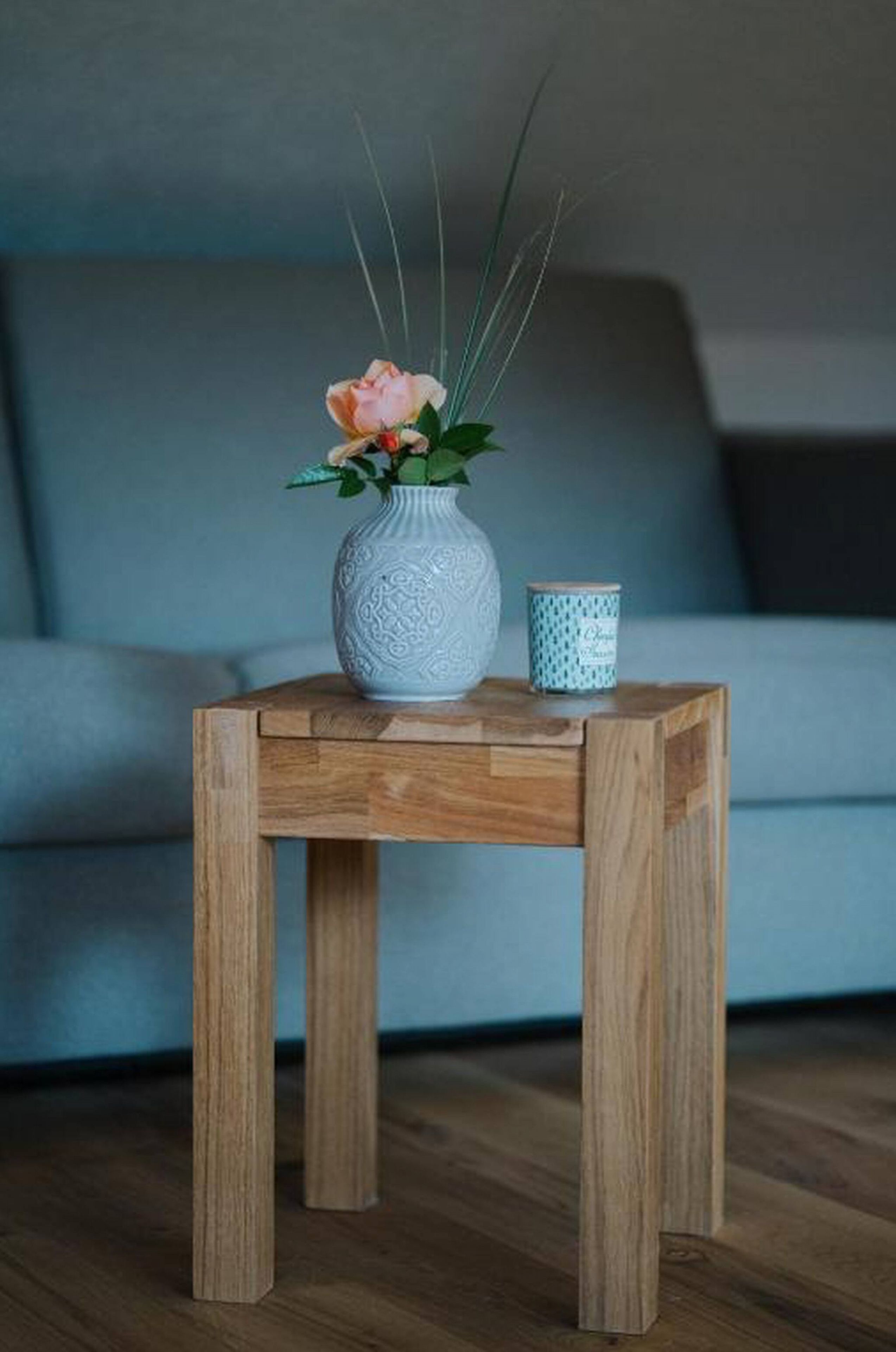Ein kleiner Holztisch mit einer weißen Vase, in der sich eine Blume und ein Kerzenständer befinden.