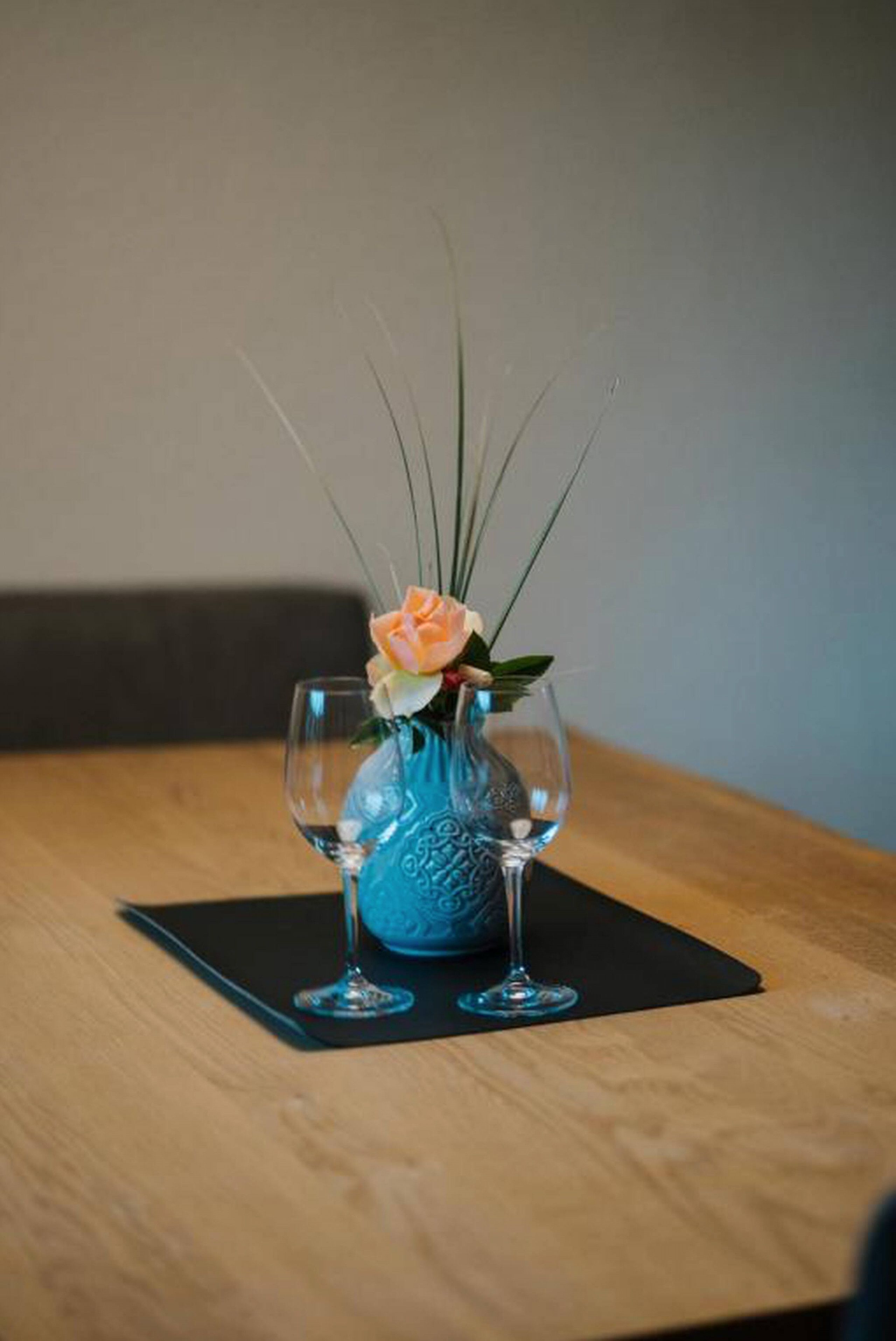 Uma mesa com um vaso azul contendo uma única flor e duas taças de vinho.