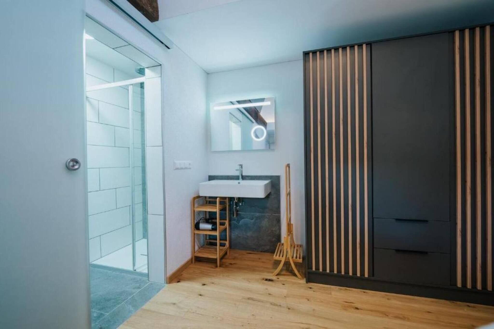 A modern bathroom with a glass shower enclosure, a wooden vanity, and a large mirror with a circular light.