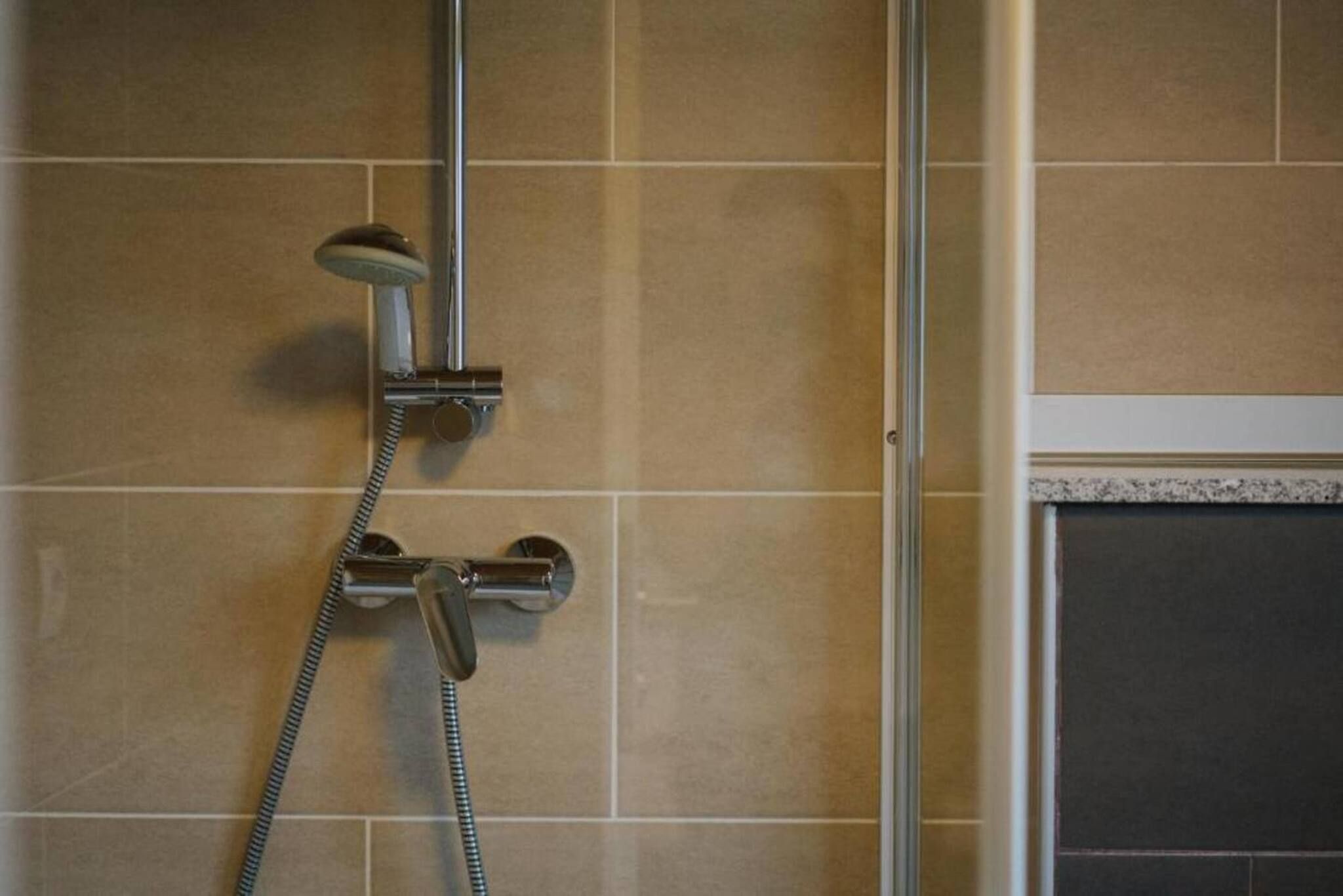A shower with a handheld showerhead and a wall-mounted faucet.