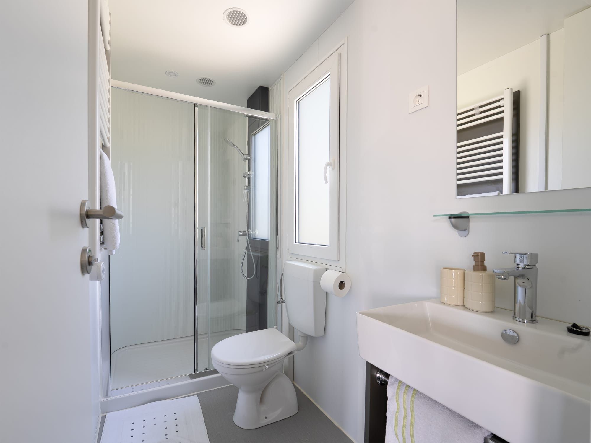 Une salle de bain moderne avec une douche à parois de verre, des toilettes, un lavabo avec un miroir et un porte-serviettes.