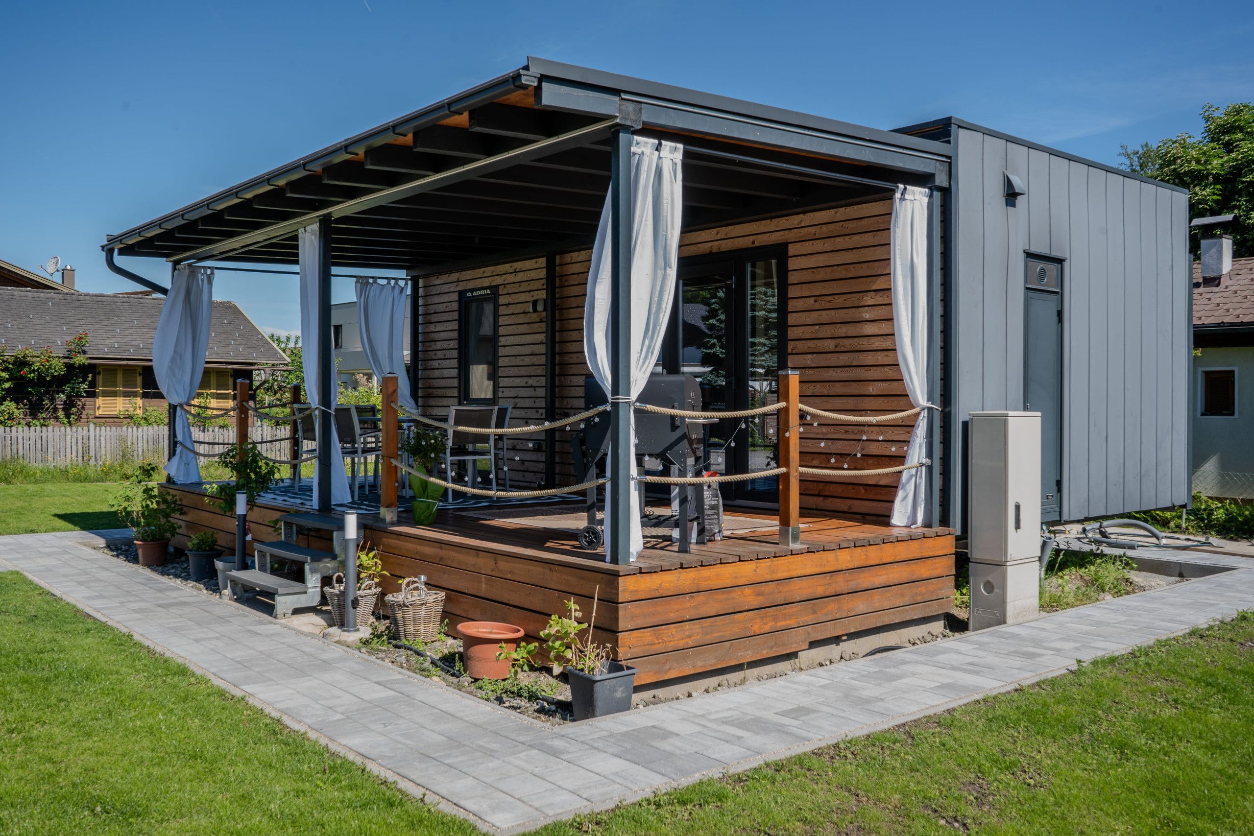 Una cabaña moderna con una terraza de madera, mobiliario exterior y un patio cubierto.