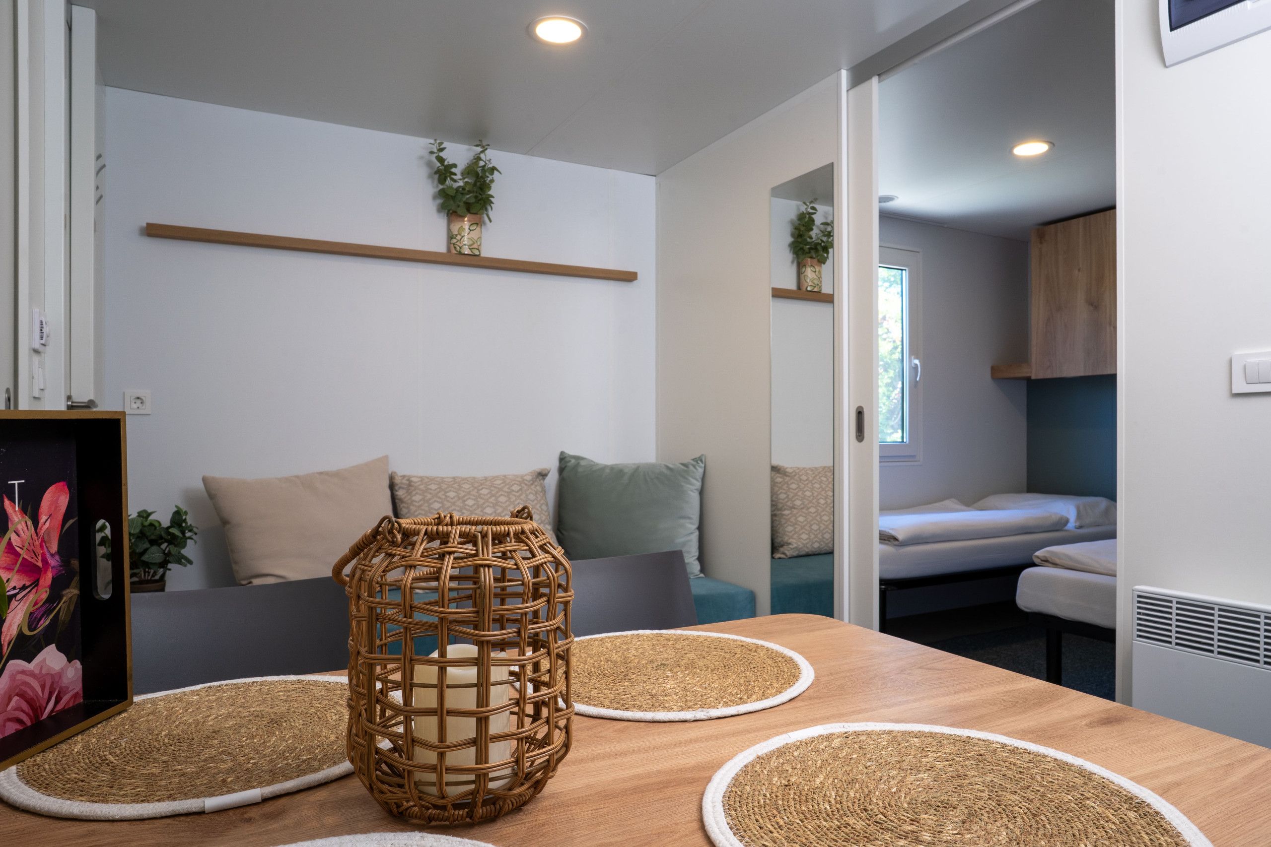 A modern, well-lit room with a wooden table, two woven placemats, a wicker basket, and a sofa with cushions.