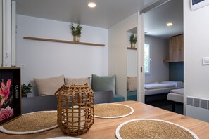 Quarto moderno e bem iluminado com uma mesa de madeira, dois jogos americanos de palha, uma cesta de vime e um sofá com almofadas.