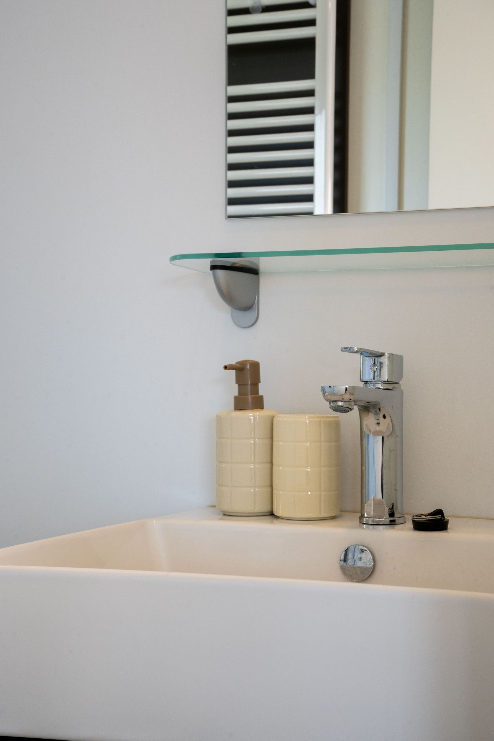 A bathroom with a white sink, a mirror, and a glass shelf above it.