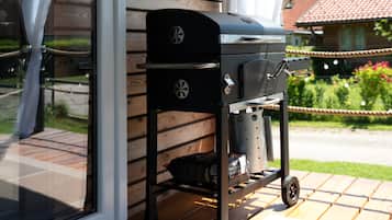 Ein Grill mit integriertem Stauraum und Rädern, platziert auf einer Holzterrasse neben einem Haus.
