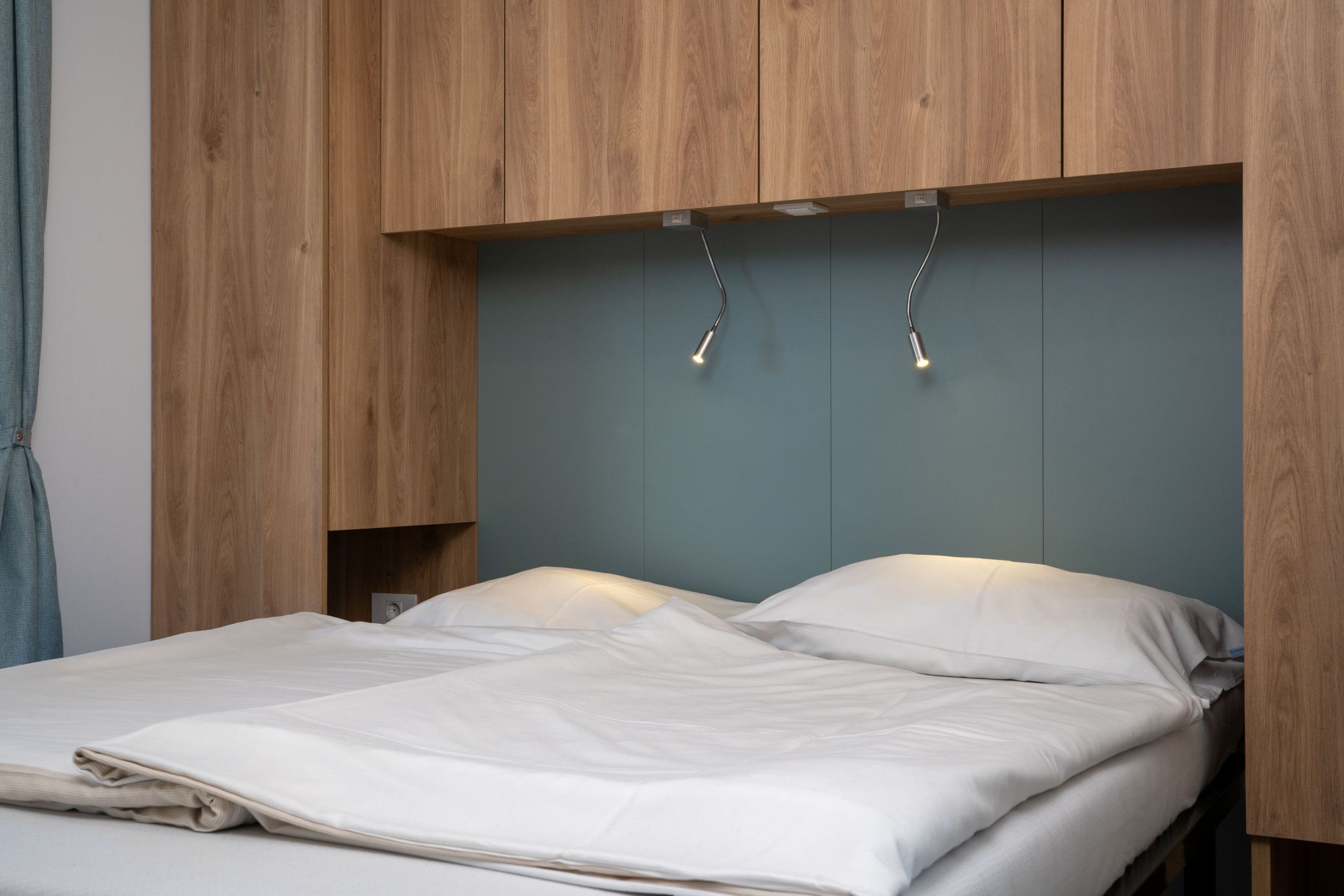 Ein Bett mit einem Holz-Kopfstück und einer grauen Wand dahinter.