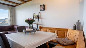 Ein gemütliches Zimmer mit einer Holzbank, einem runden Tisch mit weißem Tuch und einer Uhr an der Wand.