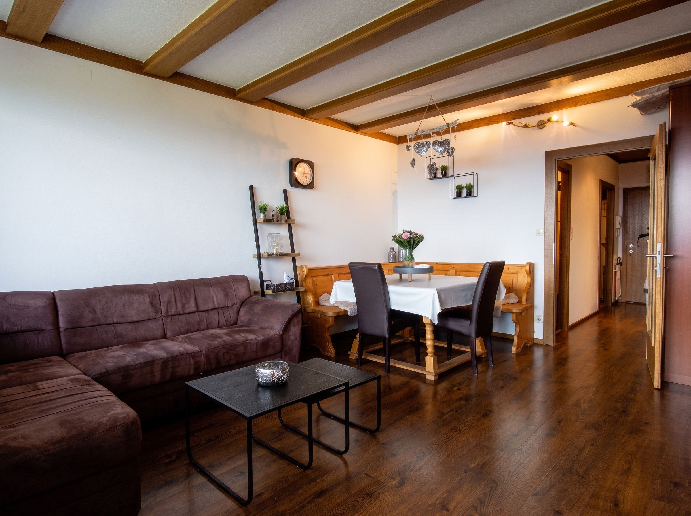 Un salon chaleureux avec un canapé en cuir marron, une petite table et un coin repas comprenant une table et des chaises en bois.